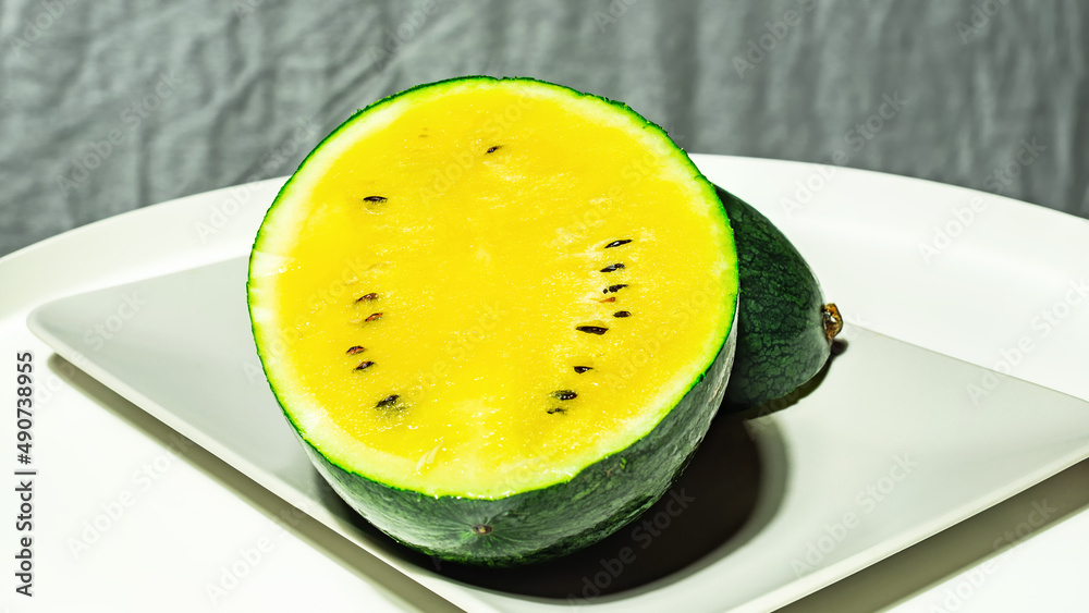 Small, fresh, bright watermelon of the Dragon's Egg variety yellow inside on a white and grey background