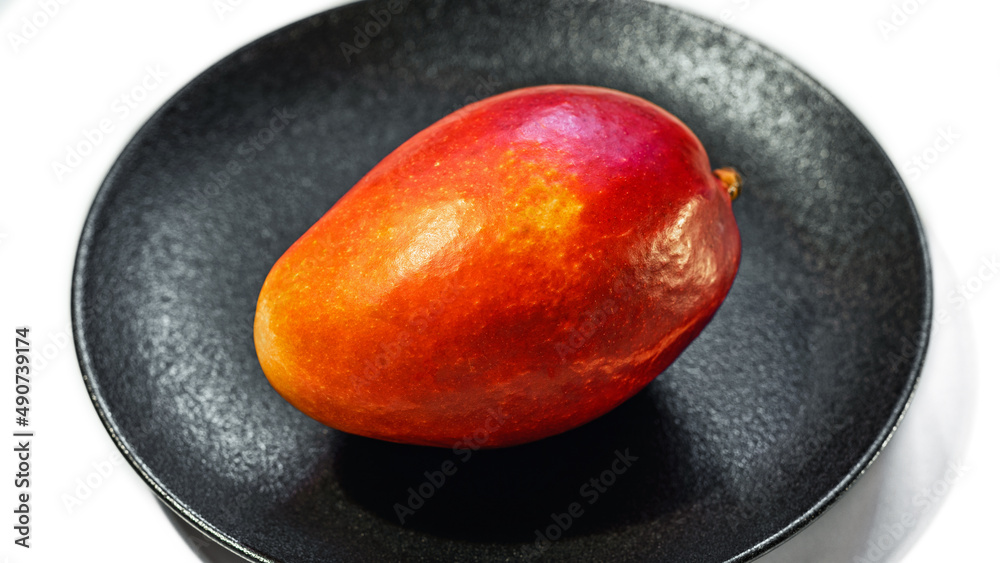 Fresh juicy red-orange mango on a black plate isolated on a white background, close-up