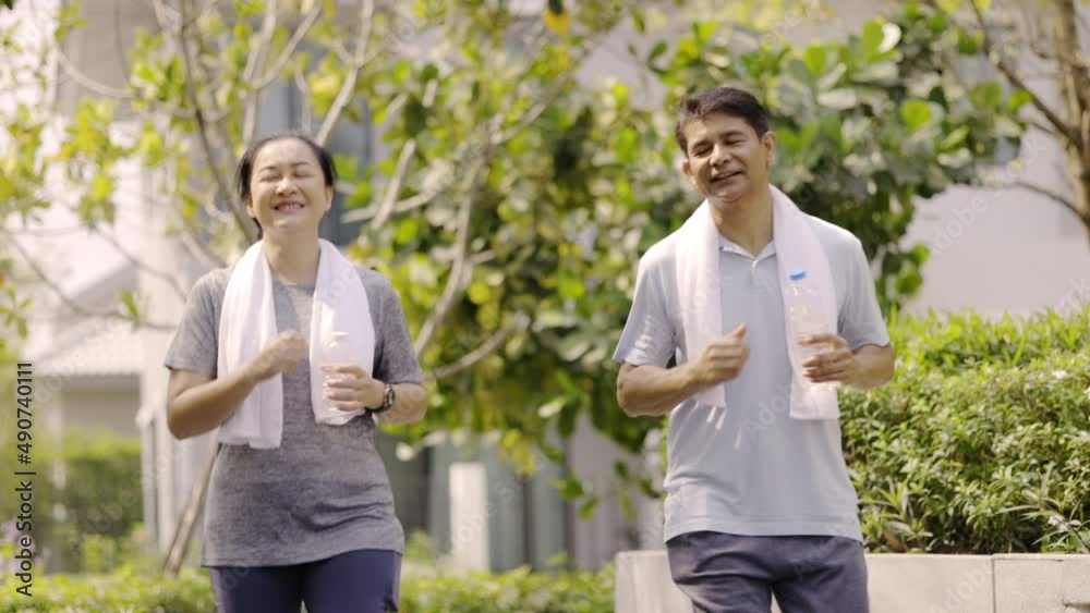 Elderly Asian couple jogging in village garden this morning smiling of happy during vacation. Retirement activities, exercise for good health. together in family life. Concept Workout and health care Elderly Asian couple jogging in village garden this morning smiling of happy during vacation. Retirement activities, exercise for good health. together in family life. Concept Workout and health care