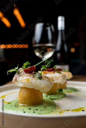 Atmospheric photo of fine dining white fish with potato, served with a glass of white wine