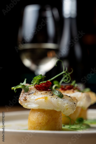 Atmospheric photo of fine dining white fish with potato, served with a glass of white wine
