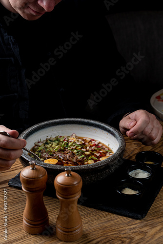 Young man is eating okroshka in a restaurant, hands are visible, dusk light, soft shadows, ad photo