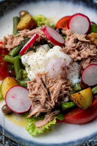 Close up of canned tuna salad with a poached egg, bright radish, lettuce and pickles are visible photo