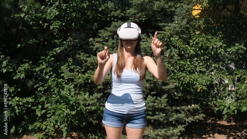 Female in virtual reality glasses controls the device with his hands against the background of green trees © Евгения Медведева