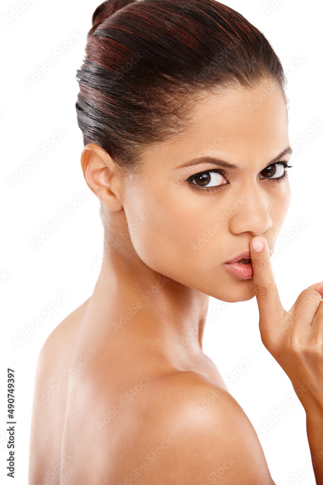 Shes not giving away her beauty secrets. Attractive young woman with her finger on her lips against a white background. Shes not giving away her beauty secrets. Attractive young woman with her finger on her lips against a white background.