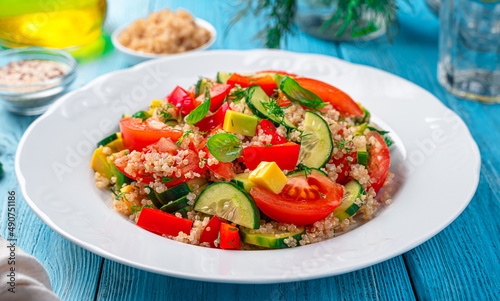 Fresh salad with vegetables, quinoa and fresh herbs on a blue background.