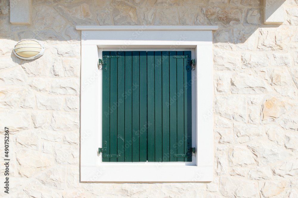 Authentic window with closed green and wooden shutters on a stone house characteristic for coastal area in Mediterranean Authentic window with closed green and wooden shutters on a stone house characteristic for coastal area in Mediterranean