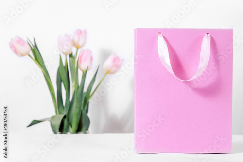 Fototapeta Naklejka Na Ścianę i Meble -  A pink gift bag with delicate tulip flowers on a white background. Discounts and sales for the spring women's holiday on the eighth of March