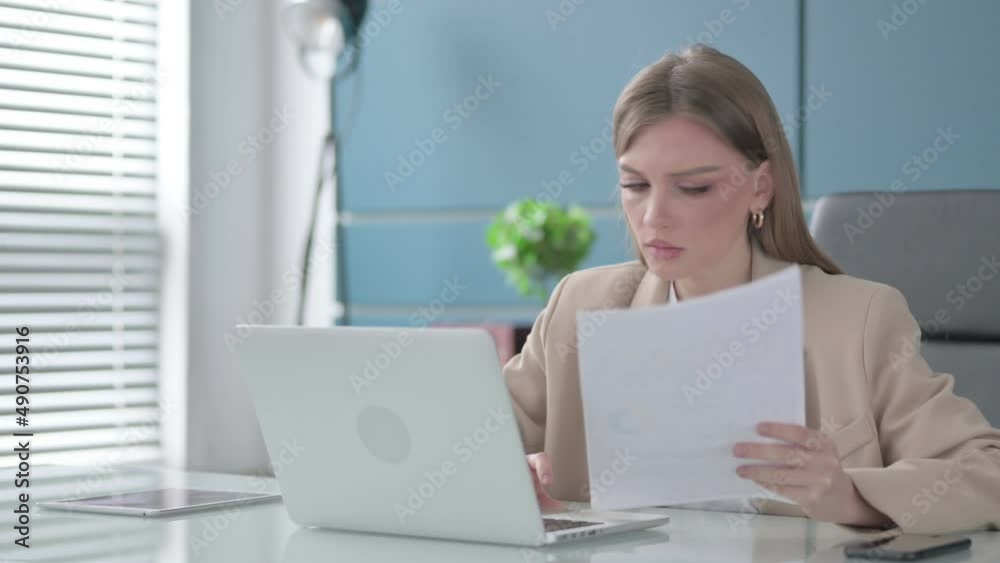 Businesswoman Reading Reports while Using Laptop Businesswoman Reading Reports while Using Laptop