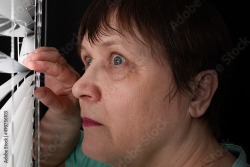 Tableau sur toile An elderly woman peers through the blinds through the window.