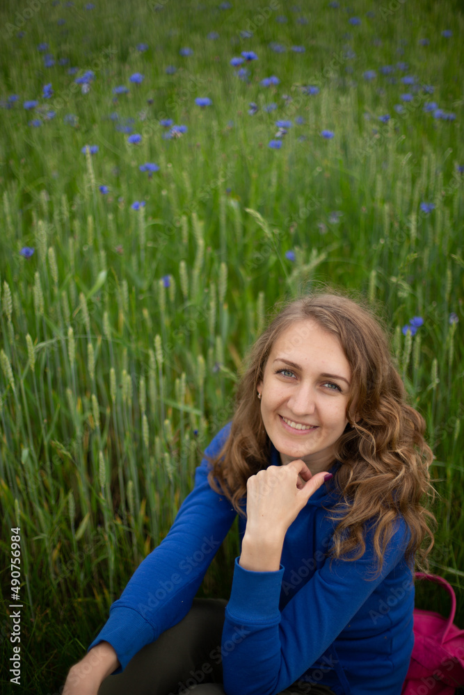 Satisfied blond girl is sitting on green grass near blue wildflowers. Women is wearing dark blue hoodie near cornflowers on the green background.
Satisfied blond girl is sitting on green grass near blue wildflowers. Women is wearing dark blue hoodie near cornflowers on the green background.