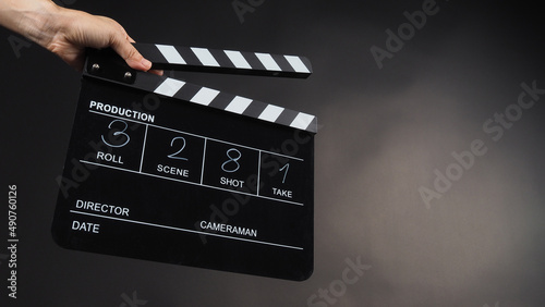 A hand is holding a black clapper board or movie slate on black background. It has been written in numbers.