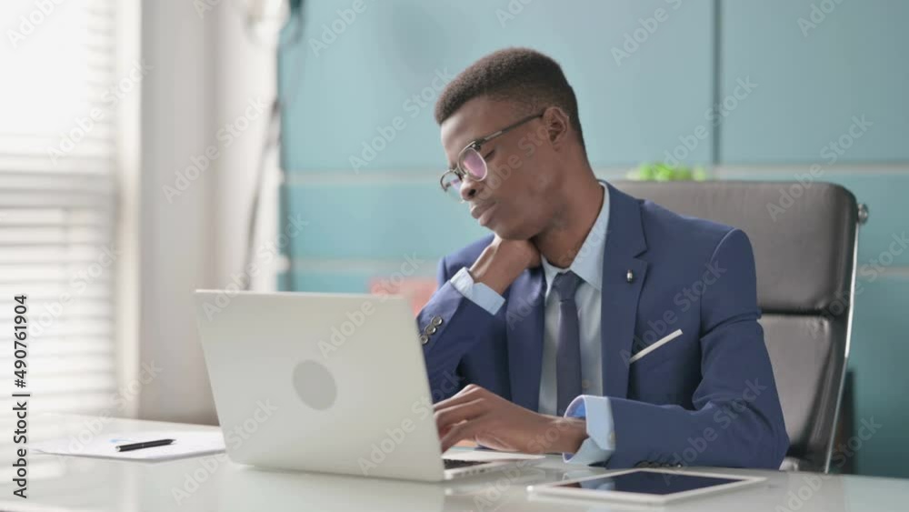 Young African Businessman having Neck Pain while using Laptop in Office Young African Businessman having Neck Pain while using Laptop in Office