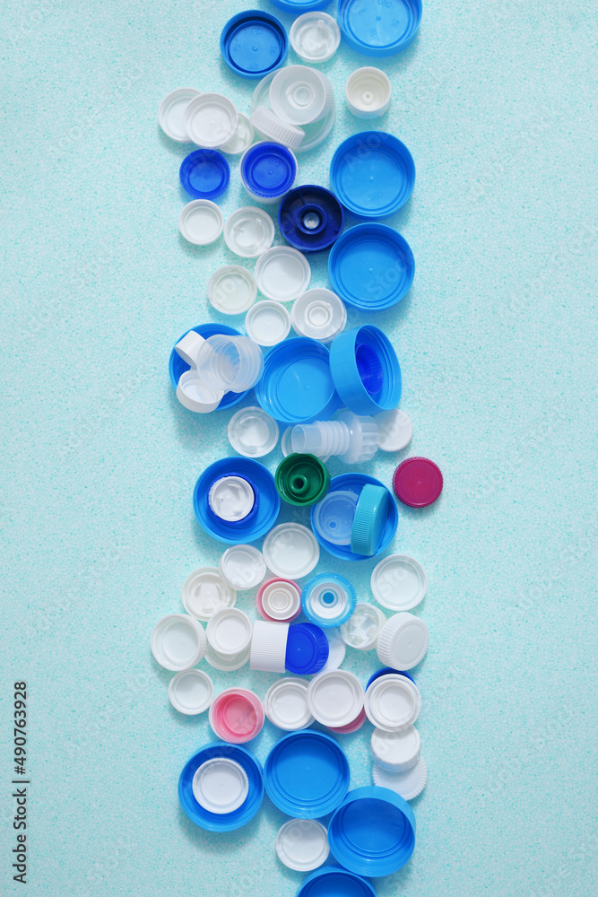 Fototapeta premium Stripe of colorated plastic bottle caps on a light blue background. View from above. 