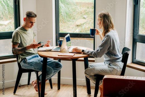 A man and a woman drink coffee in the morning at the table and work on laptops.