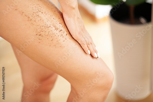 Fototapeta Beautiful young woman applying body scrub on leg at home