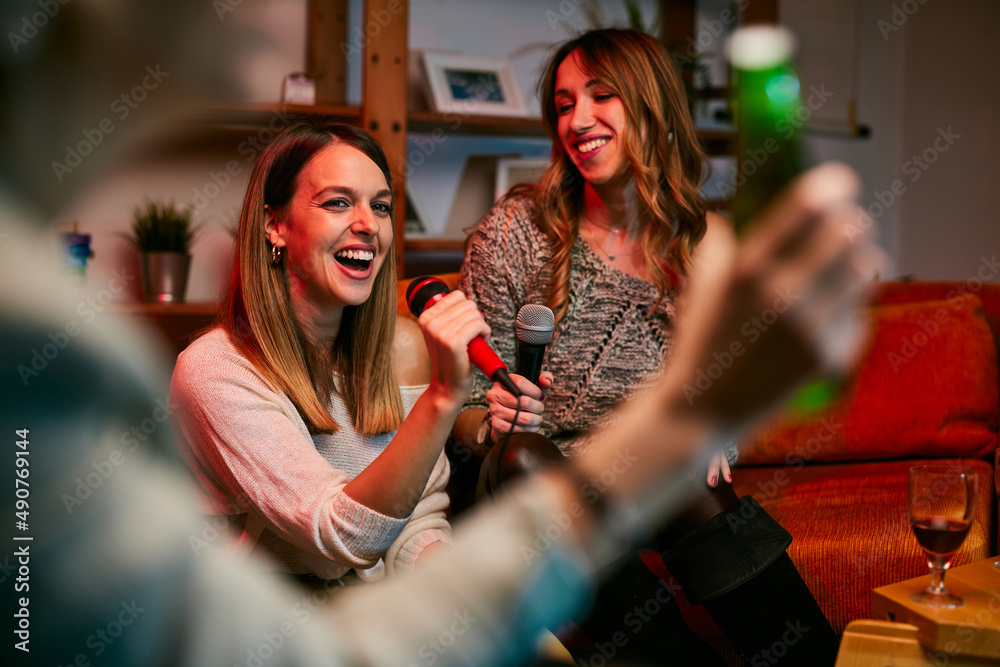 Girls sit at home, drinking and sing a duet at karaoke night.