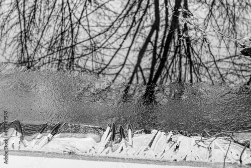 A relaxing scene of the river bank starting to freeze and reflecting the winter trees  in black and white