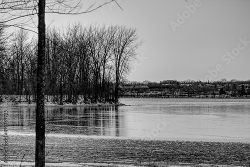 Tranquil scenery at the beginning of winter with the river partly frozen and bare trees in black and white