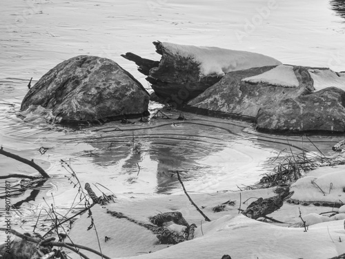 Close-up of rocks in the water, at the beginning of winter, with white snow and freezing water in black and white