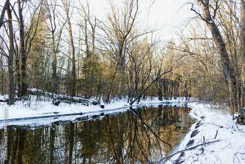 Relaxing scene in early winter, after the first snow, showing a river as a mirror reflecting the bare trees