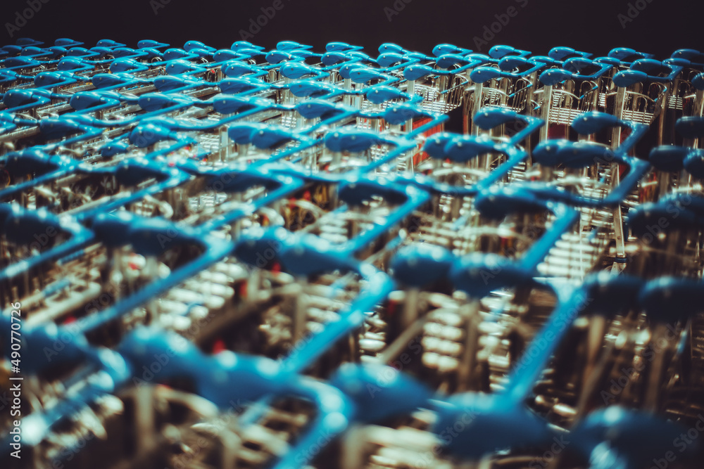 Obraz premium A huge set of luggage trolleys in a dark interior of an airport terminal; a big group of push-carts with teal handles in a shopping mall or a transport station depot, selective focus on the background