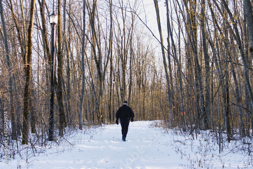 A man walking on a snowy trail, after the first snow, in a wooded area in early winter