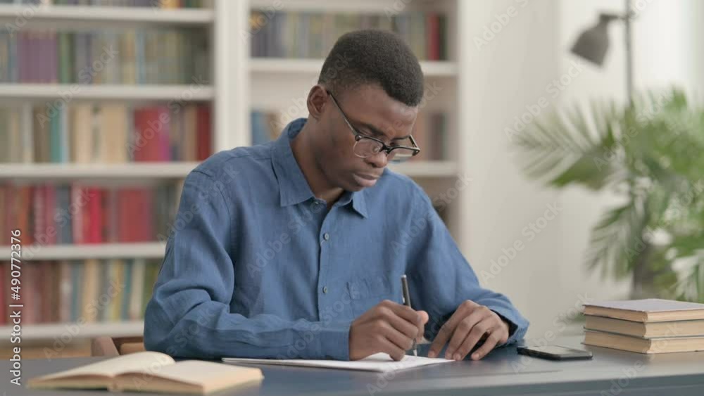 Young African Man Writing on Paper in Office Young African Man Writing on Paper in Office