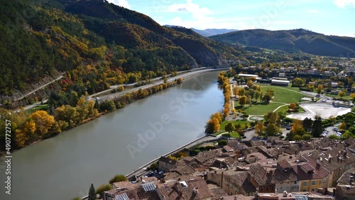 High angle view of Durance river with colorful trees in autumn season and the historic buildings of town Sisteron in Provence region, France.