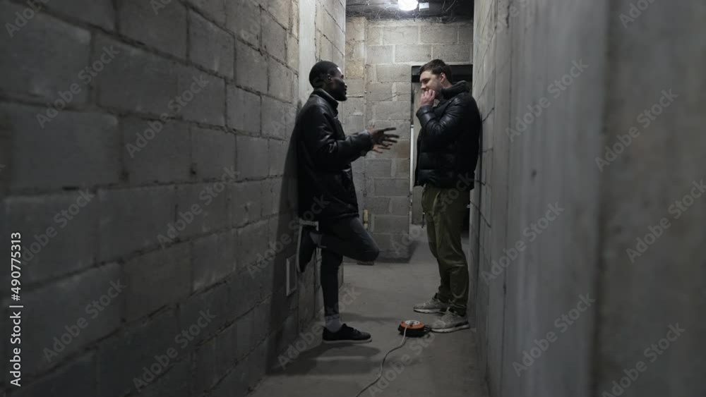 Caucasian guy and black guy are standing in a bomb-shelter and having a talk during russian invasion Caucasian guy and black guy are standing in a bomb-shelter and having a talk during russian invasion