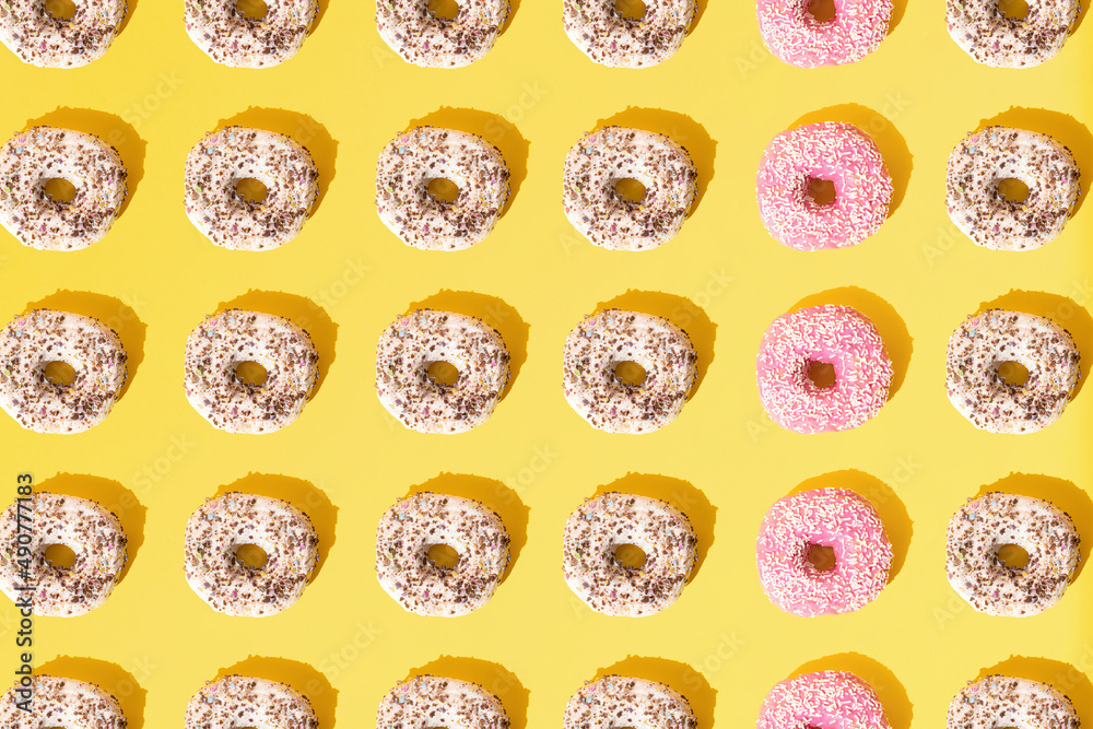 Arranged small ring donuts with white and pinl glaze. Colorful crumbs on a yellow pastel background. Pattern. Flat lay. Arranged small ring donuts with white and pinl glaze. Colorful crumbs on a yellow pastel background. Pattern. Flat lay.
