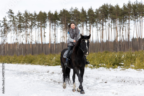 A woman riding a horse, a black horse for a walk. Favorite pet. horseback riding in winter