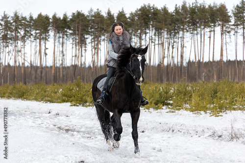 A woman riding a horse, a black horse for a walk. Favorite pet. horseback riding in winter