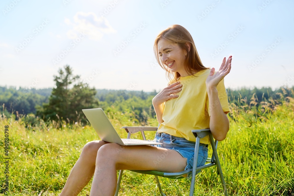 Summer vacation in wild meadow, adult woman resting on folding chair for camping using laptop Summer vacation in wild meadow, adult woman resting on folding chair for camping using laptop