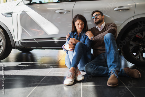 Fotografía A sad young couple sits next to a car in a car dealership because they can't afford the car they want