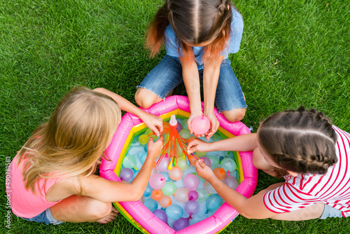 Water balloon games for kids. Close up of girls filling up water balloons at sunny day. Summer fun outdoor activities for children concept