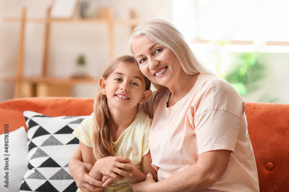Little girl with her grandmother hugging on sofa at home