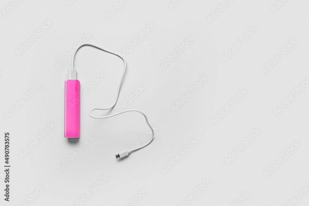 Pink power bank with USB cable on light background
