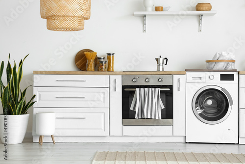 Interior of light kitchen with washing machine, oven and white counter photo