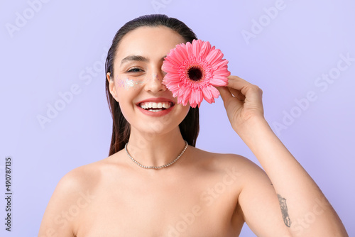 Happy woman with creative makeup closing face with gerbera flower on color background