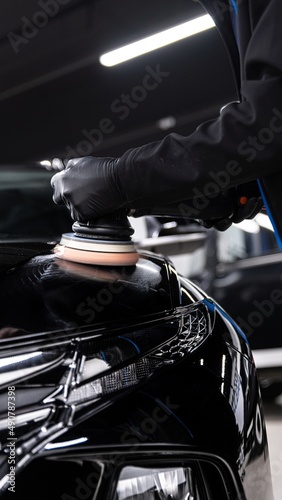 Car detailing studio technician polishing black car paint with eletric polisher