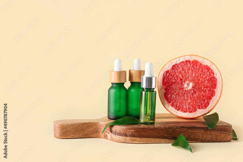 Wooden board with bottles of essential oil and grapefruit on color background Wooden board with bottles of essential oil and grapefruit on color background