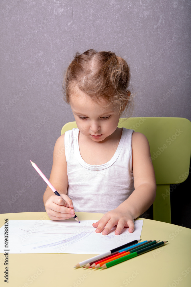 a little girl draws with colored pencils while sitting at a table a little girl draws with colored pencils while sitting at a table