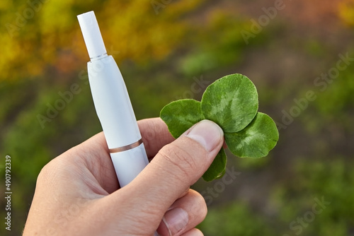 A woman holds an electronic cigarette and a lucky four-leaf clover in her hand. The concept of successful smoking cessation. Quit smoking. The choice between smoking and health. Symbol of good luck. photo