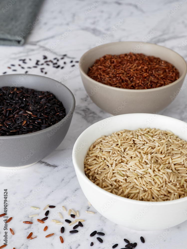 Rice of different colors: brown, red and black in a bowl. Assortment of rice grains on marble table. Rice of different colors: brown, red and black in a bowl. Assortment of rice grains on marble table.