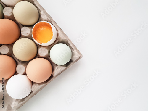 farm eggs are natural colored in an egg tray on a white background. one is broken