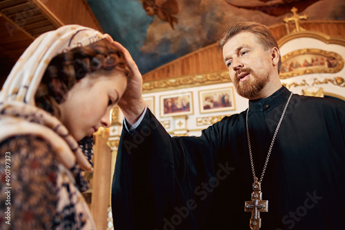a priest blesses a teenage girl in a headscarf in an Orthodox church after a festive church mass