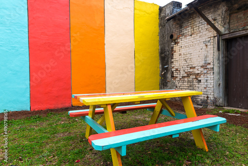 Fotografering Colorful picnic table with benches on the grass against a painted wall