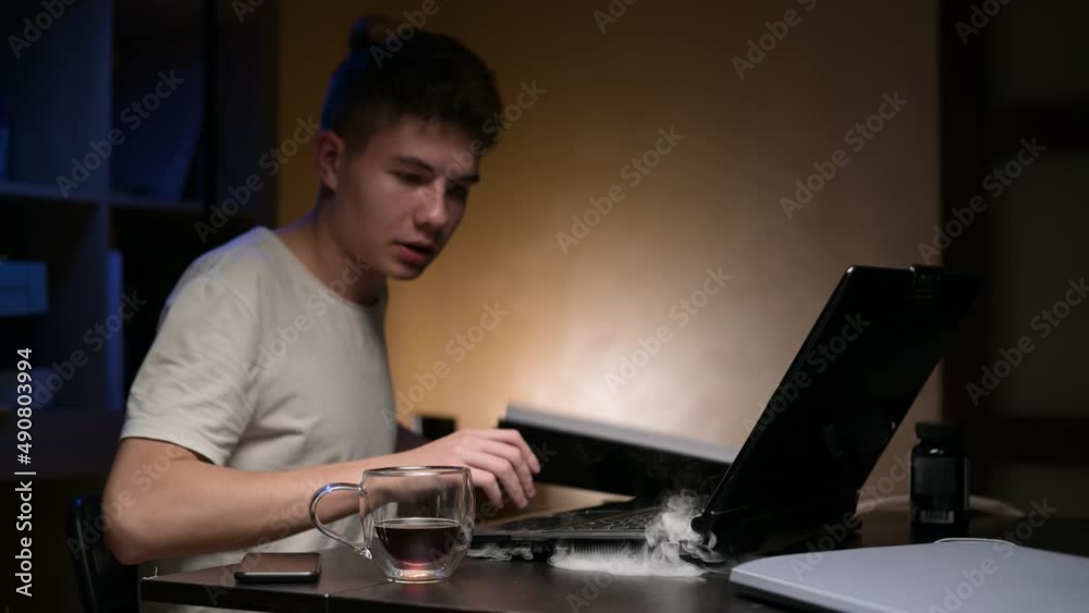 A young man's laptop starts to smoke while he is working. The guy is in a panic trying to deal with the situation. Death of an old laptop while working A young man's laptop starts to smoke while he is working. The guy is in a panic trying to deal with the situation. Death of an old laptop while working