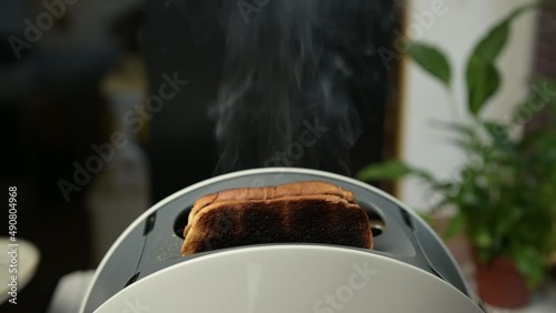 Burnt slices of bread fly out of the toaster, which is smoking. Toast burnt due to broken old toaster. bad morning photo